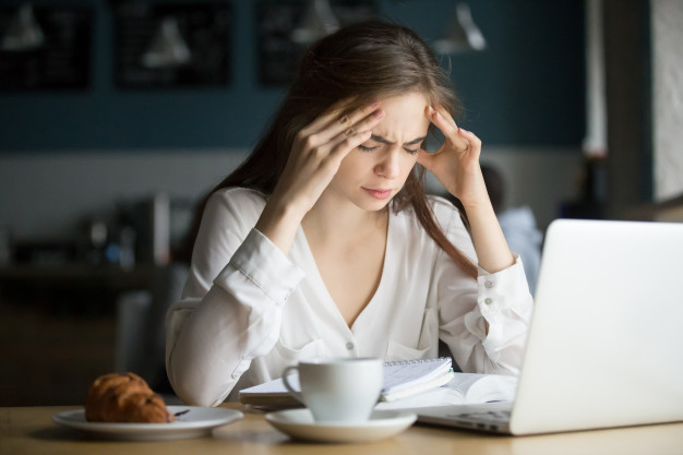 Caucasian woman having a headache while doing work in front of a laptop