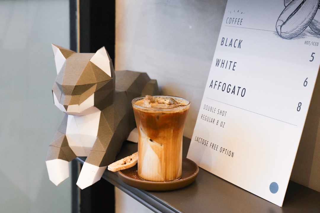 Iced Latte at Clap Cafe, in front of their coffee menu and cat decor